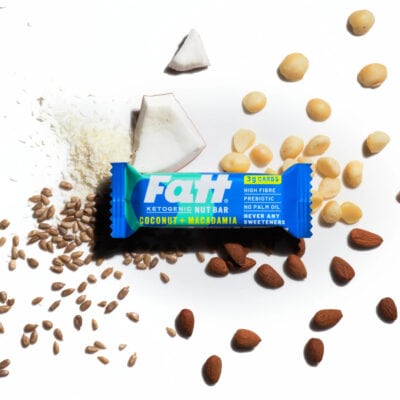 Fatt - Coconut + Macadamia bar on a white background with coconut, almonds and macadamia nuts spread out behind it.
