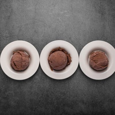 three scoops of chocolate keto fat bombs on white plates on a black kitchen counter