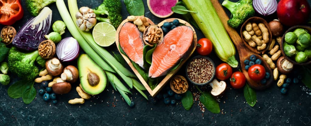 Keto friendly foods including salmond, nuts, broccoli, mushrooms and more on a black slate