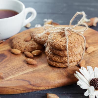 low-carb oatmeal biscuits in a stack on a wooden slab with a cup of tea in the background. white flower in the foreground
