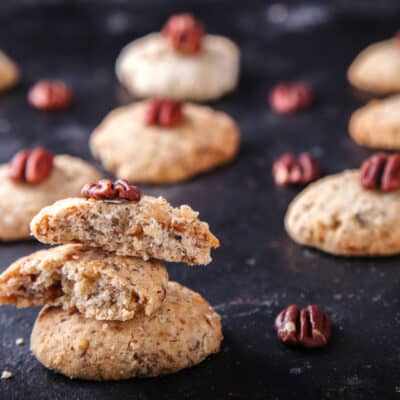 11 Low-Carb Pecan Sandies Biscuits on a black slate cover with pecans spread around.