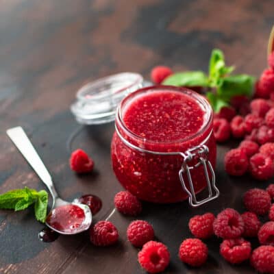 low crab rasberry jam in a clear jar on a wooden table, one teaspoon with jam on and some scattered raspberries