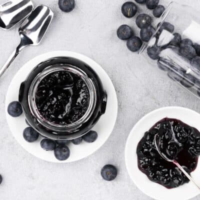 blueberry jam in a clear bowl and on a plate. Two spoons and some fresh blueberries in a glass