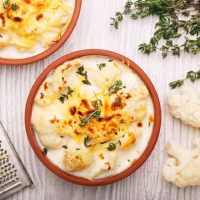 Low-carb cauliflower cheese in a brown baking dish with thyme sprinkled over