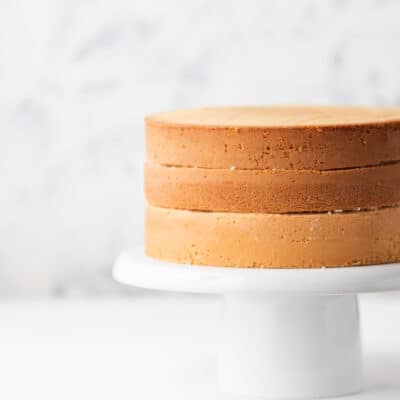 3 low carb victoria sponge cakes stacked on a white cake stand on a white counter top