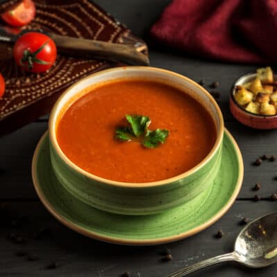 low-carb tomato soup in a green bowl on a black kitchen table. three tomatoes in the background