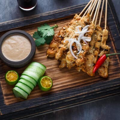 low-carb malaysian satay chicken on a wooden board with a peanut butter dipping sauce