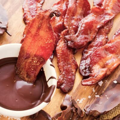 strips of cooked bacon on a chopping board, with one strip half way dipped in melted low-carb chocolate