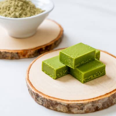 3 keto matcha fat bombs on a wooden plate, with a bowl of matcha powder in the background