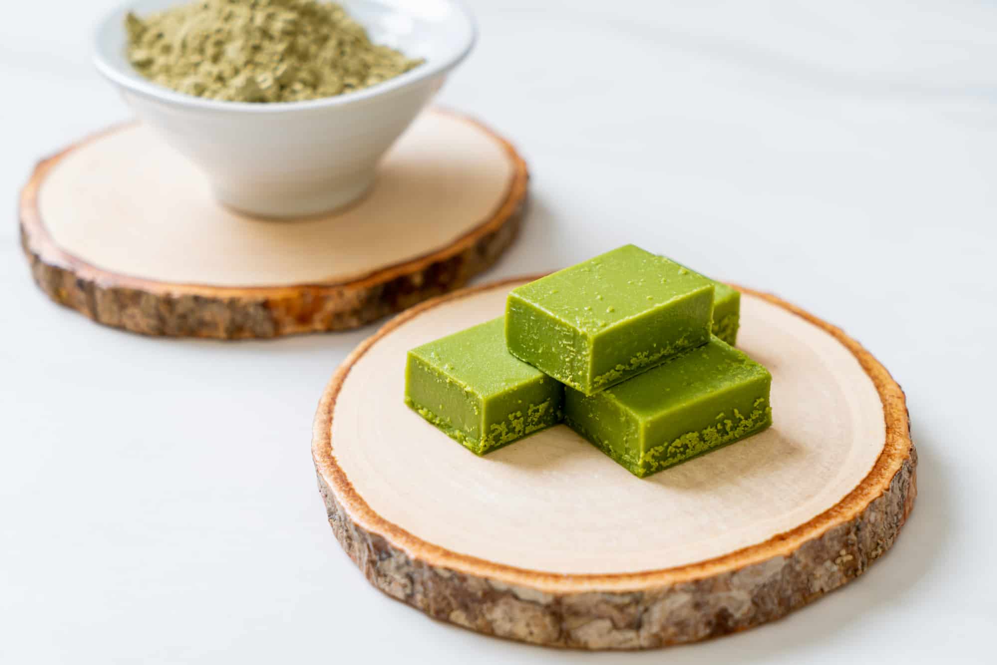 3 keto matcha fat bombs on a wooden plate, with a bowl of matcha powder in the background